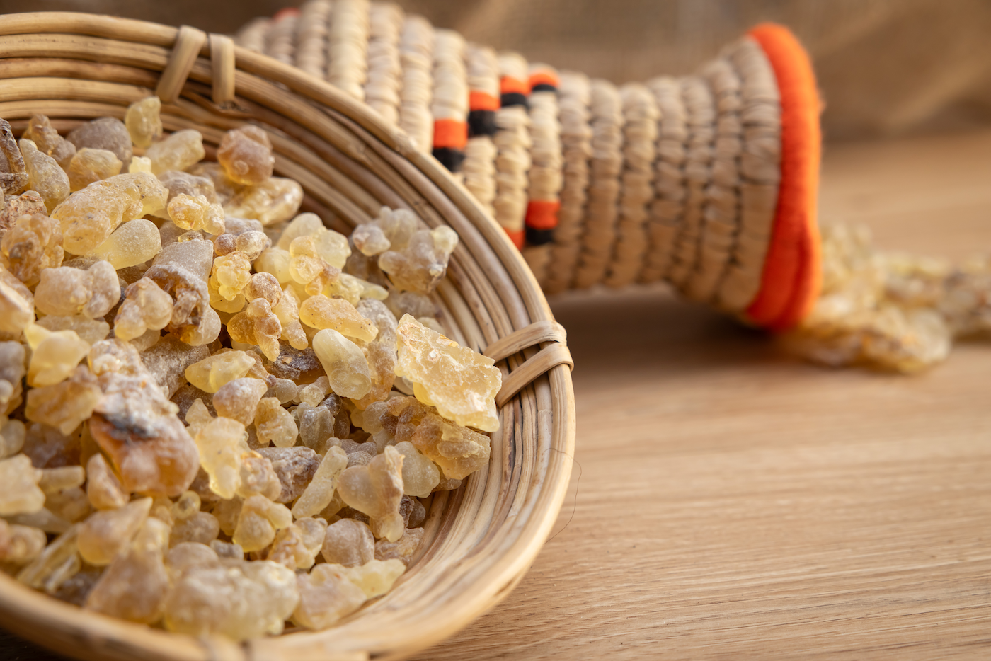 Basket of frankincense resin on a wooden surface with a woven container in the background.