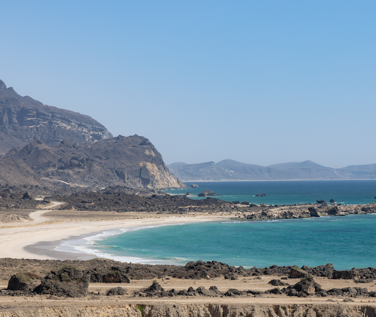 Beach with rocky shoreline and mountains in the background in Oman
