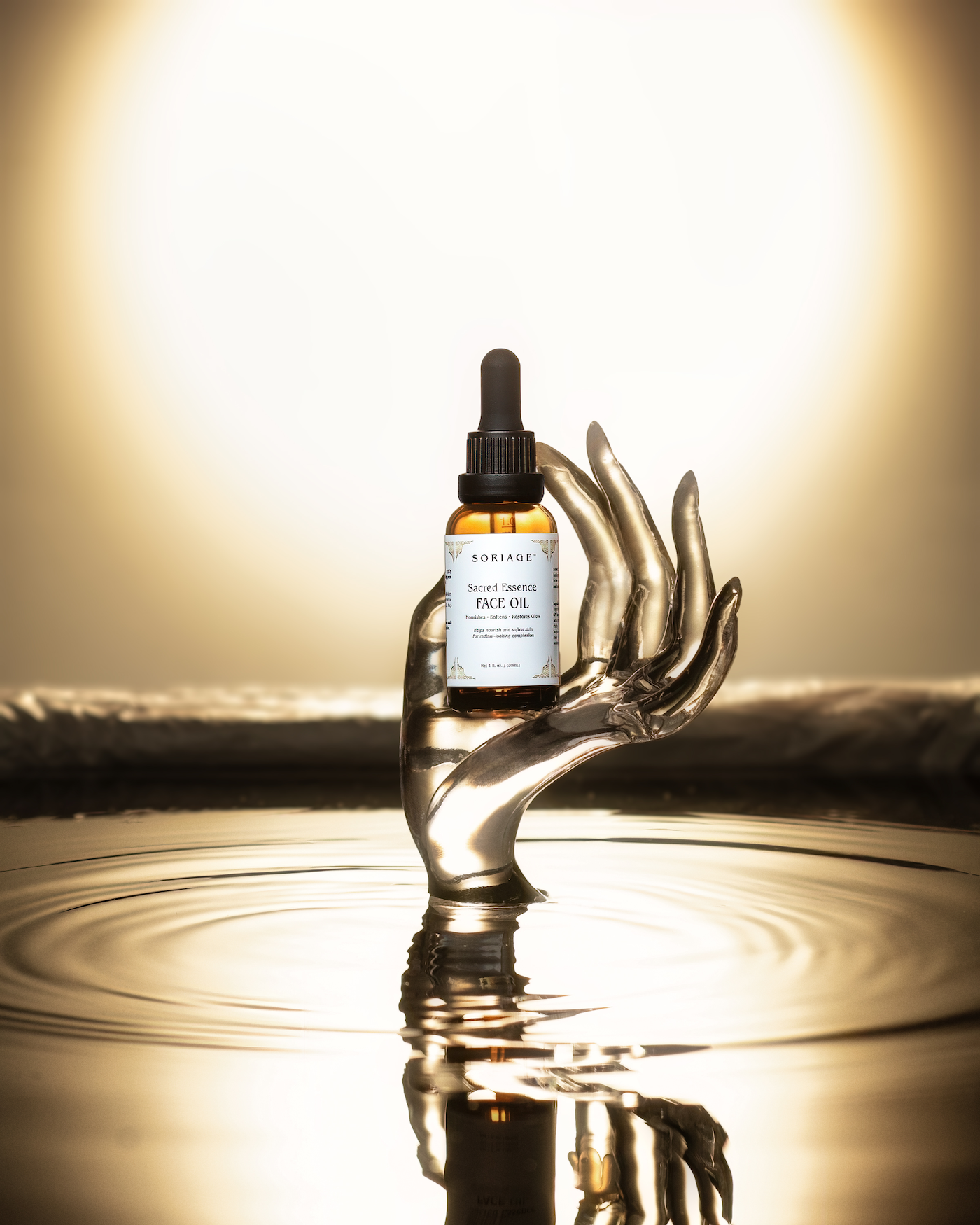 Acrylic hand coming out of oil holding the Sacred Essence Face Oil bottle and a soft glow in the background